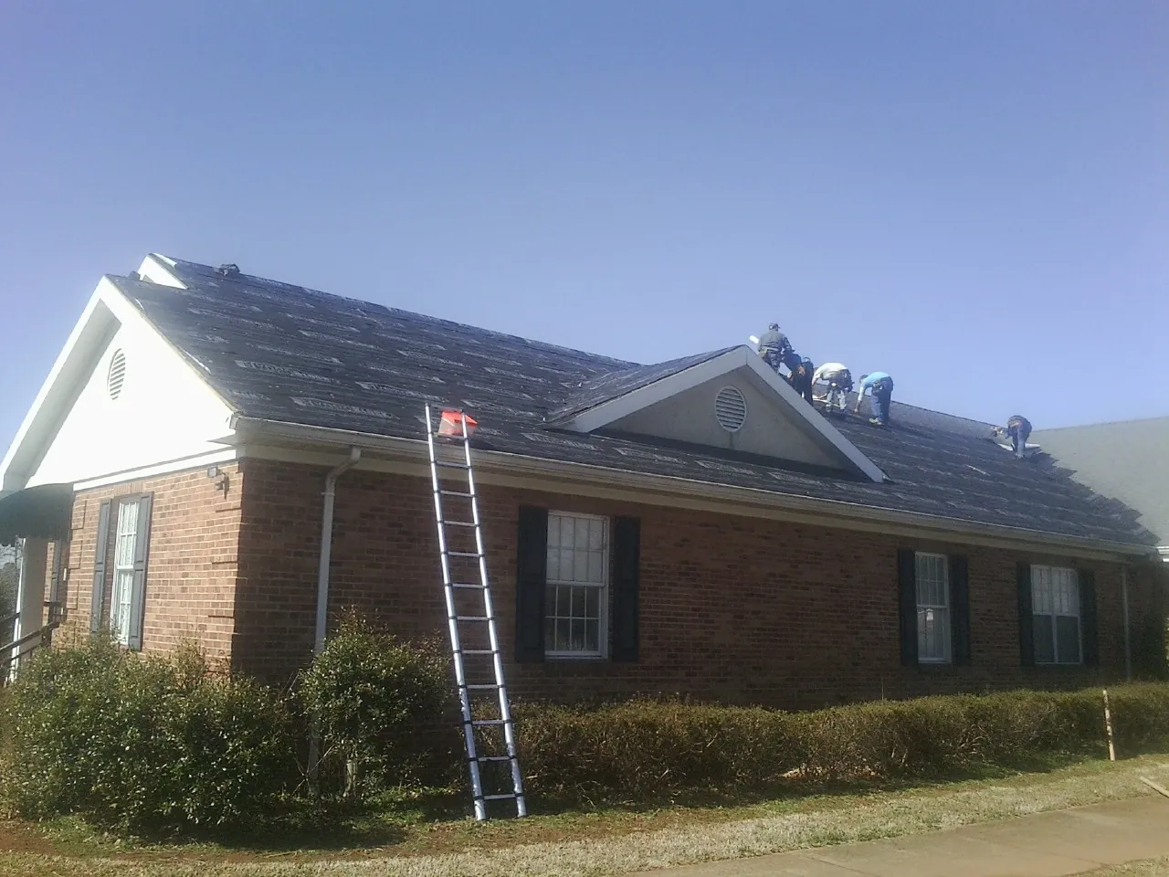 Crew tearing shingles off a brick ranch roof with a ladder set — Emergency Roof Repair work by our crew in Quarryville