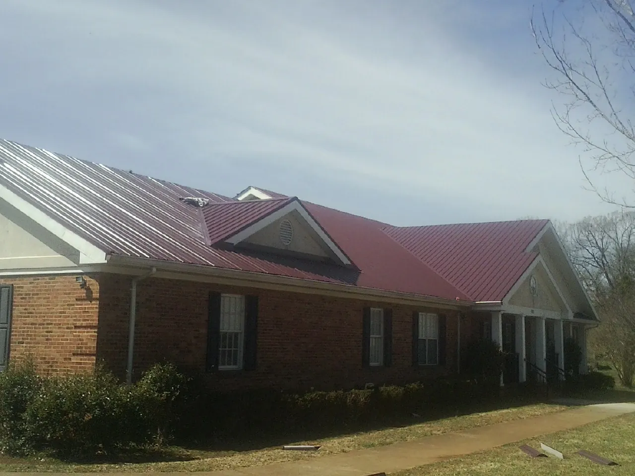 Red metal roof with gabled entries on a long brick building, from a Hail Damage Roof Repair job in Quarryville