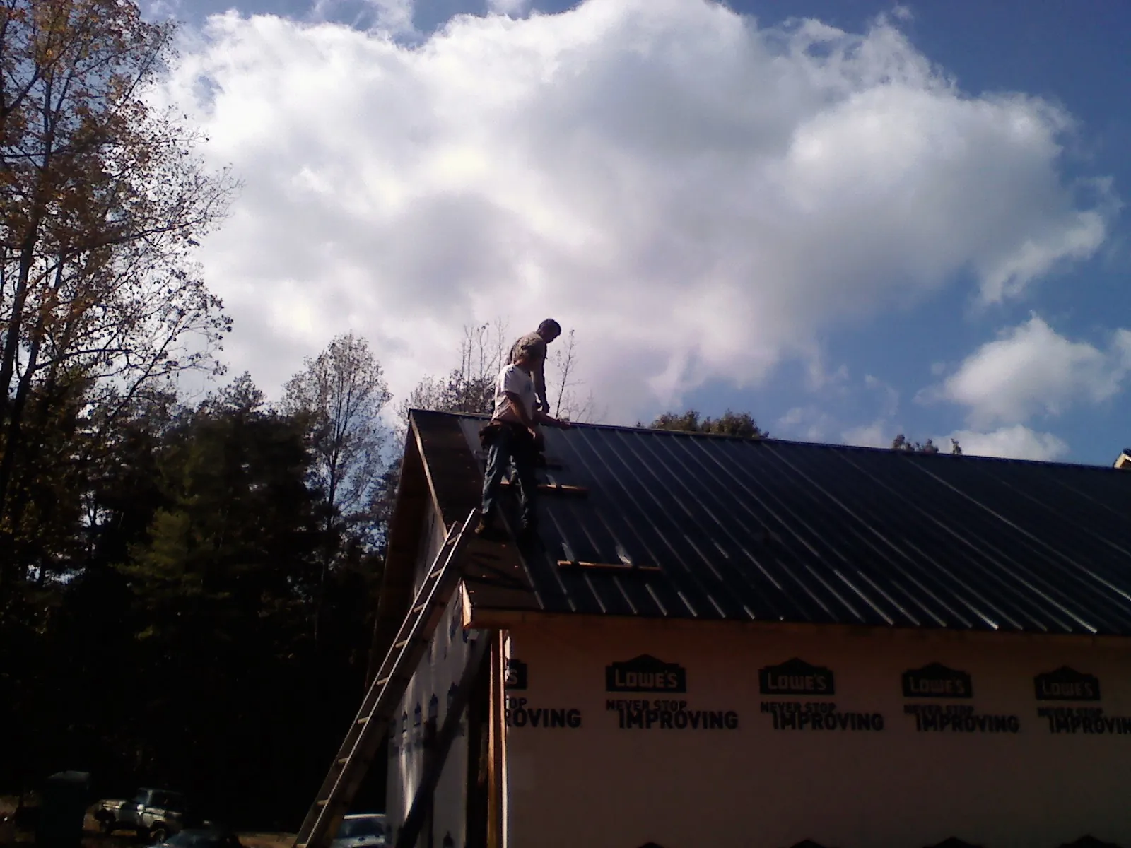 Roofer fastening dark metal panels high against a cloudy sky, from a Roof Inspection job in Quarryville