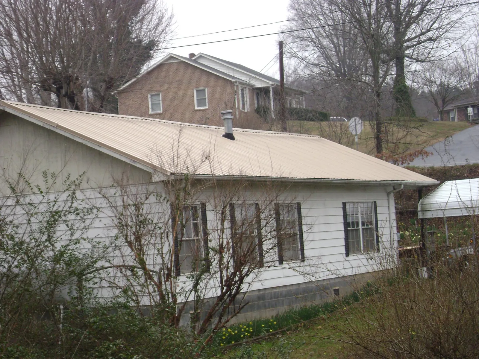 Tan metal roof on a white sided house set into a hillside — Commercial Roofing by Roofing Brothers in Quarryville